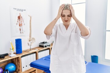 Young caucasian woman working at pain recovery clinic suffering from headache desperate and stressed because pain and migraine. hands on head.