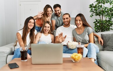 Group of young friends having video call using laptop sitting on the sofa at home.