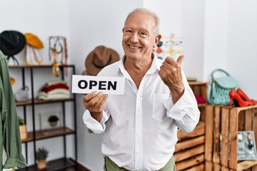 Senior man holding banner with open text at retail shop pointing thumb up to the side smiling happy with open mouth