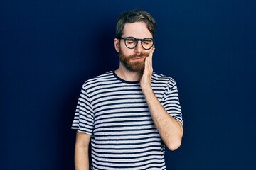 Caucasian man with beard wearing striped t shirt and glasses touching mouth with hand with painful expression because of toothache or dental illness on teeth. dentist