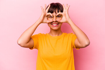 Young hispanic woman isolated on pink background showing okay sign over eyes