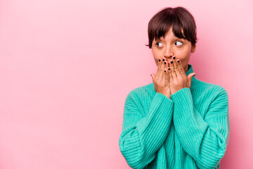 Young hispanic woman isolated on pink background thoughtful looking to a copy space covering mouth with hand.