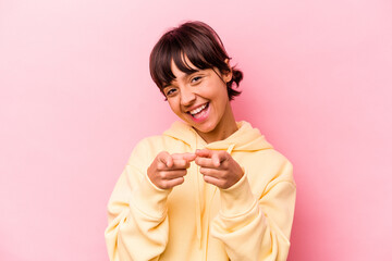 Young hispanic woman isolated on pink background pointing to front with fingers.