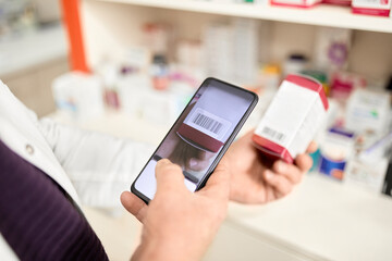Pharmacist scanning barcode of medicine box through smart phone at pharmacy store