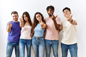 Group of young people standing together over isolated background showing middle finger, impolite...