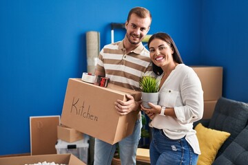 Man and woman couple holding kitchen package and plant pot standing at new home