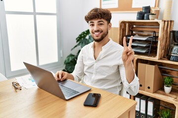 Young arab man working using computer laptop at the office smiling with happy face winking at the...