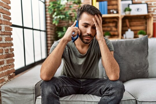Young hispanic man worried talking on the smartphone at home