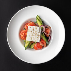 Fresh Greek salad - feta cheese, tomatoes, cucumber, red pepper, black olives and onion on a black background.