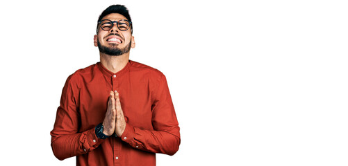 Young hispanic man with beard wearing business shirt and glasses begging and praying with hands...