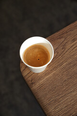 Top view of a paper cup of black coffee on wooden table