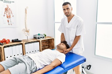 Obraz premium Two hispanic men physiotherapist and patient having rehab session massaging head at clinic