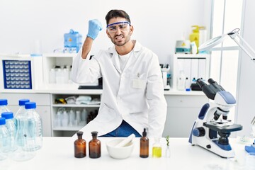 Young hispanic man working at scientist laboratory annoyed and frustrated shouting with anger, yelling crazy with anger and hand raised