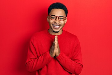 Young african american man wearing casual clothes and glasses praying with hands together asking...