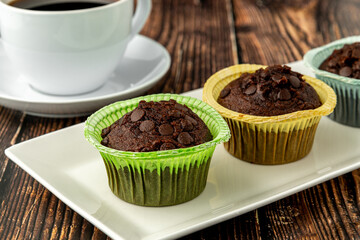 Chocolate chip and cocoa muffins in colorful muffin paper molds on wooden table