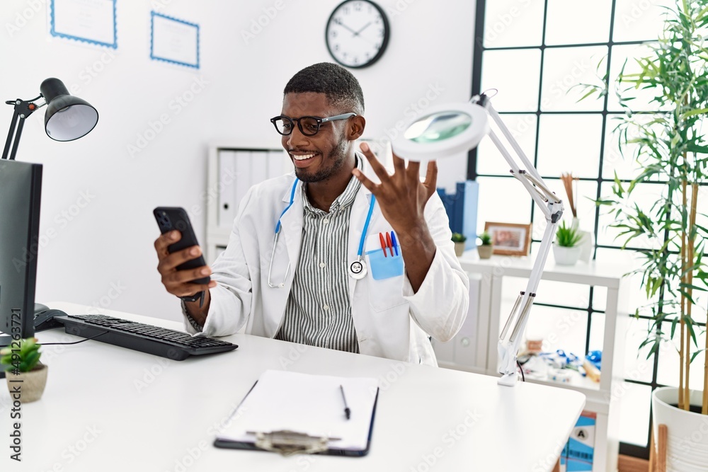 Wall mural Young african american man wearing doctor uniform having video call at clinic