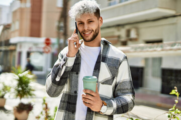 Young hispanic man talking smartphone drinking coffee at the city.