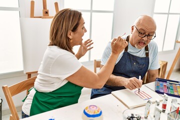 Obraz premium Middle age hispanic painter couple smiling happy playing to paint face with paintbrush at art studio.