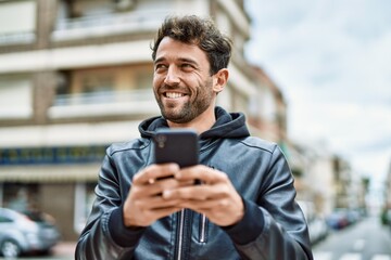 Handsome hispanic man with beard smiling happy outdoors using smartphone
