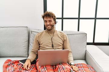 Young handsome man with beard wearing operator headset working from home winking looking at the...