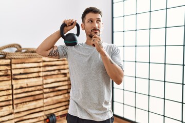 Young handsome man wearing sportswear using dumbbells serious face thinking about question with...