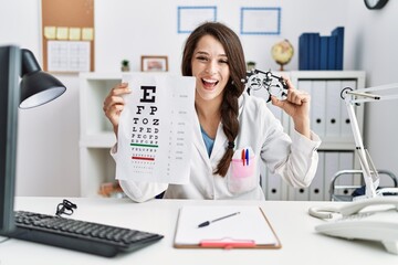 Young doctor woman holding optometry glasses and eyesight test at the clinic smiling and laughing...