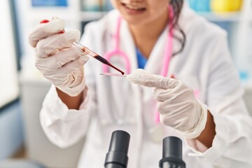 Young chinese woman wearing scientist uniform analysing blood at laboratory