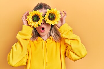 Beautiful caucasian woman holding yellow sunflowers over eyes afraid and shocked with surprise and...