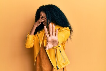Middle age african american woman wearing wool winter sweater and leather jacket covering eyes with hands and doing stop gesture with sad and fear expression. embarrassed and negative concept.