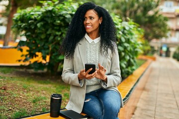 Middle age african american businesswoman using smartphone and drinking coffee at the park.