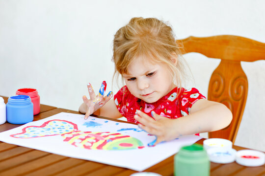 Little creative toddler girl painting with finger colors a fish. Active child having fun with drawing at home, in kindergaten or preschool. Education and distance learning for kids. Creaitve activity.