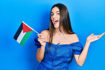 Young brunette teenager holding palestine flag celebrating achievement with happy smile and winner expression with raised hand
