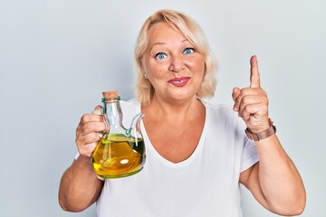 Middle age blonde woman holding olive oil can smiling with an idea or question pointing finger with...