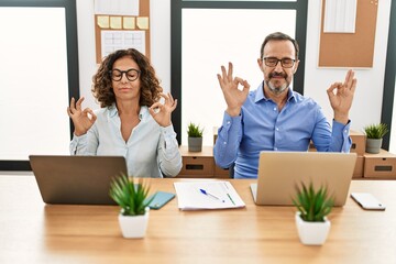 Fototapeta premium Middle age hispanic woman and man sitting with laptop at the office relax and smiling with eyes closed doing meditation gesture with fingers. yoga concept.