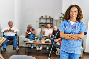 Obraz premium Middle age doctor woman smiling happy standing with arms crossed gesture at nursing home.