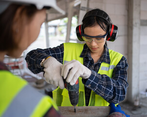 Female Civil engineer from Asia is using an electric screwdriver and wearing personal protective equipment.
Worker Wear a helmet, hard hat, gloves, safety glasses,Ear muff.Work safe concept.Prevention