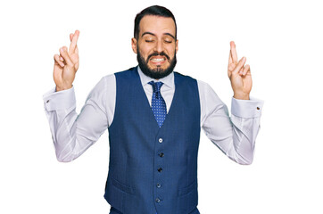 Young man with beard wearing business vest gesturing finger crossed smiling with hope and eyes closed. luck and superstitious concept.