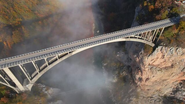 Aerial video of the magnificent Djurdjevica Bridge over the Tara river canyon in the northern part of Montenegro. Beautiful morning fog moves through the arches of the bridge. Shot in the fall season