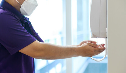 Male hands using automatic alcohol gel dispenser for cleaning hand and clear bacteria for stop Covid 19 virus outbreak. Protection against the corona virus 2019. Save and clean in public building.