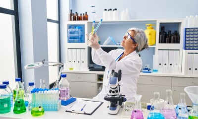 Middle age woman wearing scientist uniform looking test tubes at laboratory