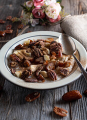 Breakfast bowl with porridge,  pecan nuts, dates, bananas, apples and cinnamon