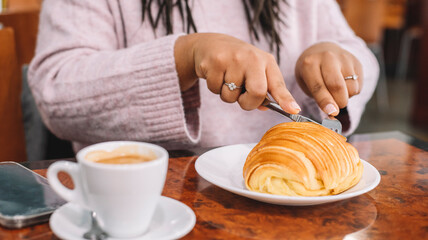 Young woman having breakfast with croissant and coffee