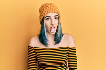 Young modern girl wearing wool hat sticking tongue out happy with funny expression. emotion concept.