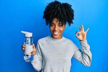 African american woman with afro hair drinking bottle of water doing ok sign with fingers, smiling friendly gesturing excellent symbol