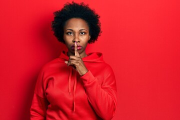 Young african american woman wearing casual sweatshirt asking to be quiet with finger on lips. silence and secret concept. - obrazy, fototapety, plakaty