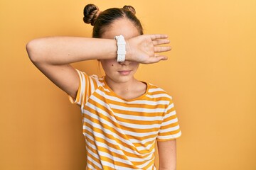 Beautiful brunette little girl wearing casual striped t shirt covering eyes with arm, looking serious and sad. sightless, hiding and rejection concept