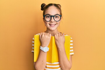 Beautiful brunette little girl wearing glasses and holding book smiling with a happy and cool smile on face. showing teeth.