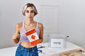 Young beautiful woman at political campaign election holding canada flag thinking attitude and...