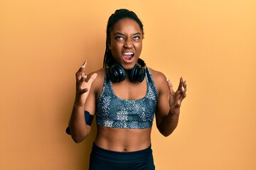 African american woman with braided hair wearing sportswear and arm band crazy and mad shouting and yelling with aggressive expression and arms raised. frustration concept.