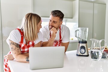 Young couple smiling confident using laptop looking smoothie recipe at kitchen